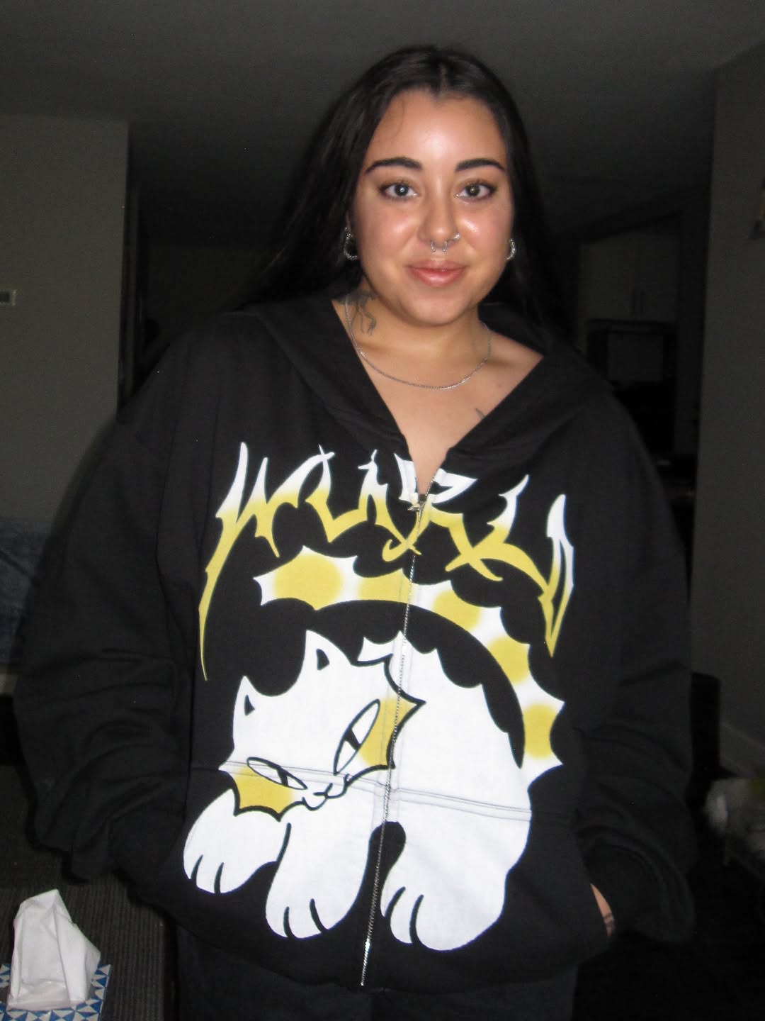 White and yellow cat character with black outlines and text on upper arm, displayed on person wearing black hoodie.