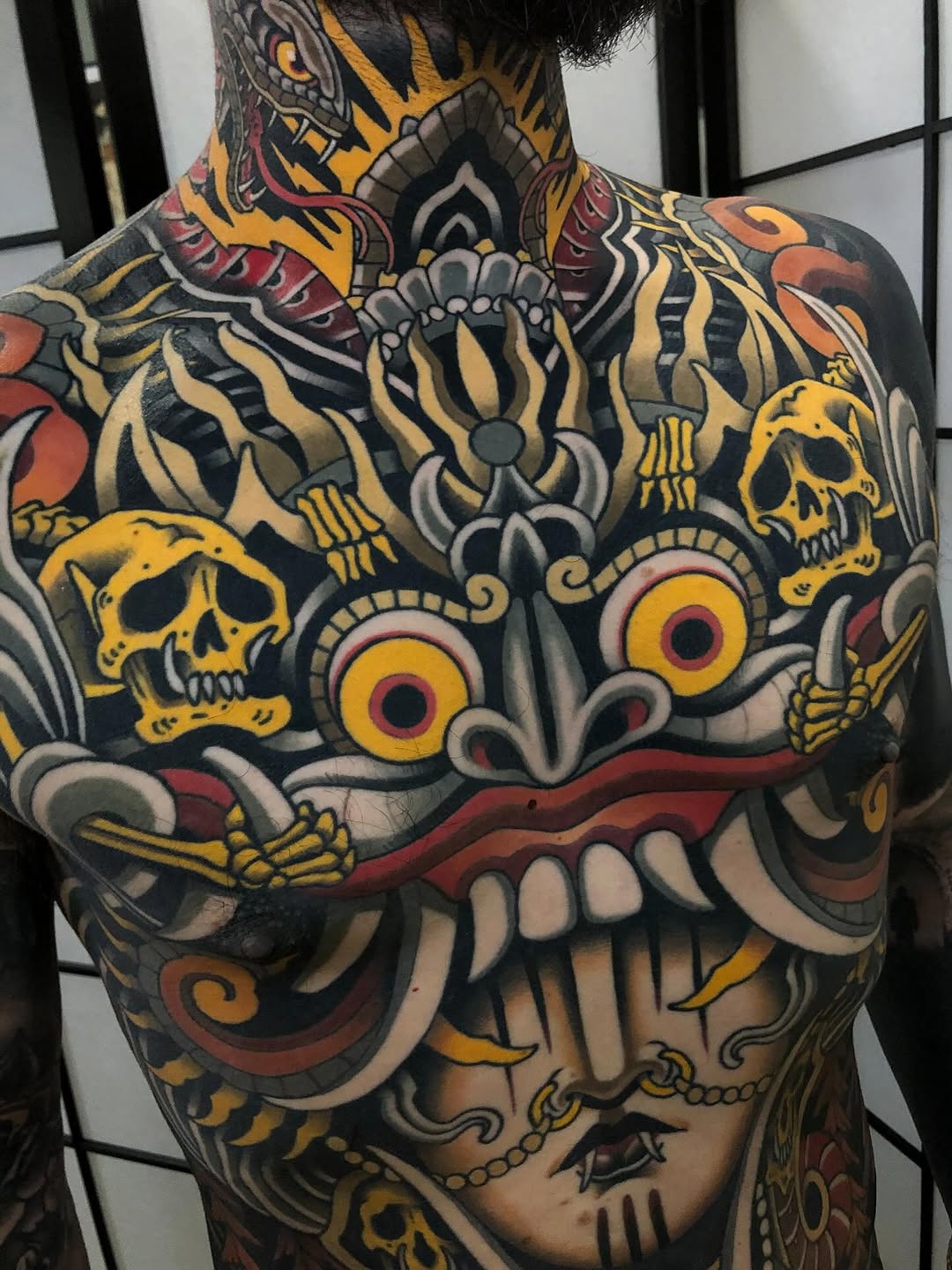 Large colorful back tattoo featuring skulls, ornamental flowers, and decorative elements in yellow, red, black, and gold tones.