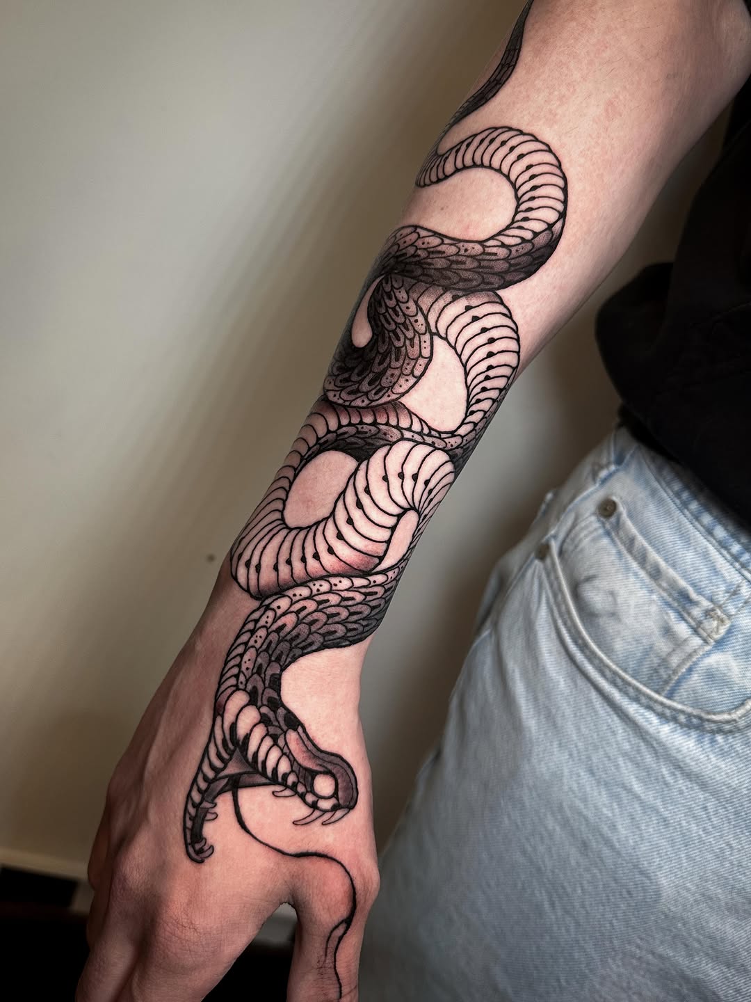 Intricate black ink serpent and tentacle design wrapping around forearm and hand with detailed scales and segmented patterns.