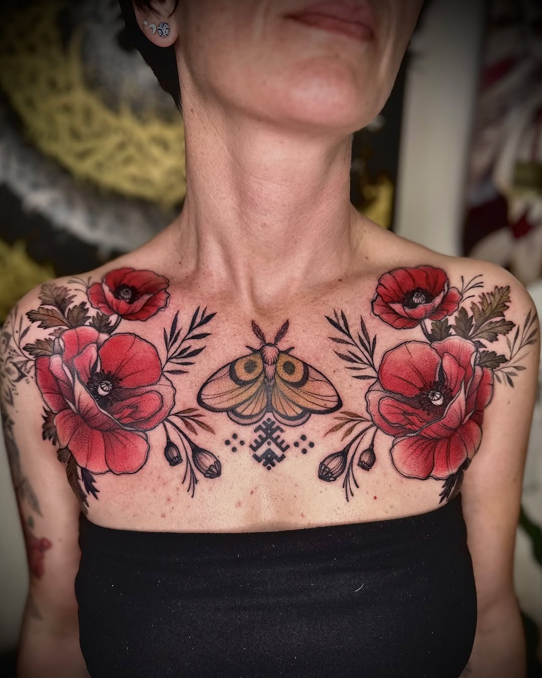 Chest tattoo featuring symmetrical red poppies with black botanical details and a central moth design surrounded by ornamental elements.