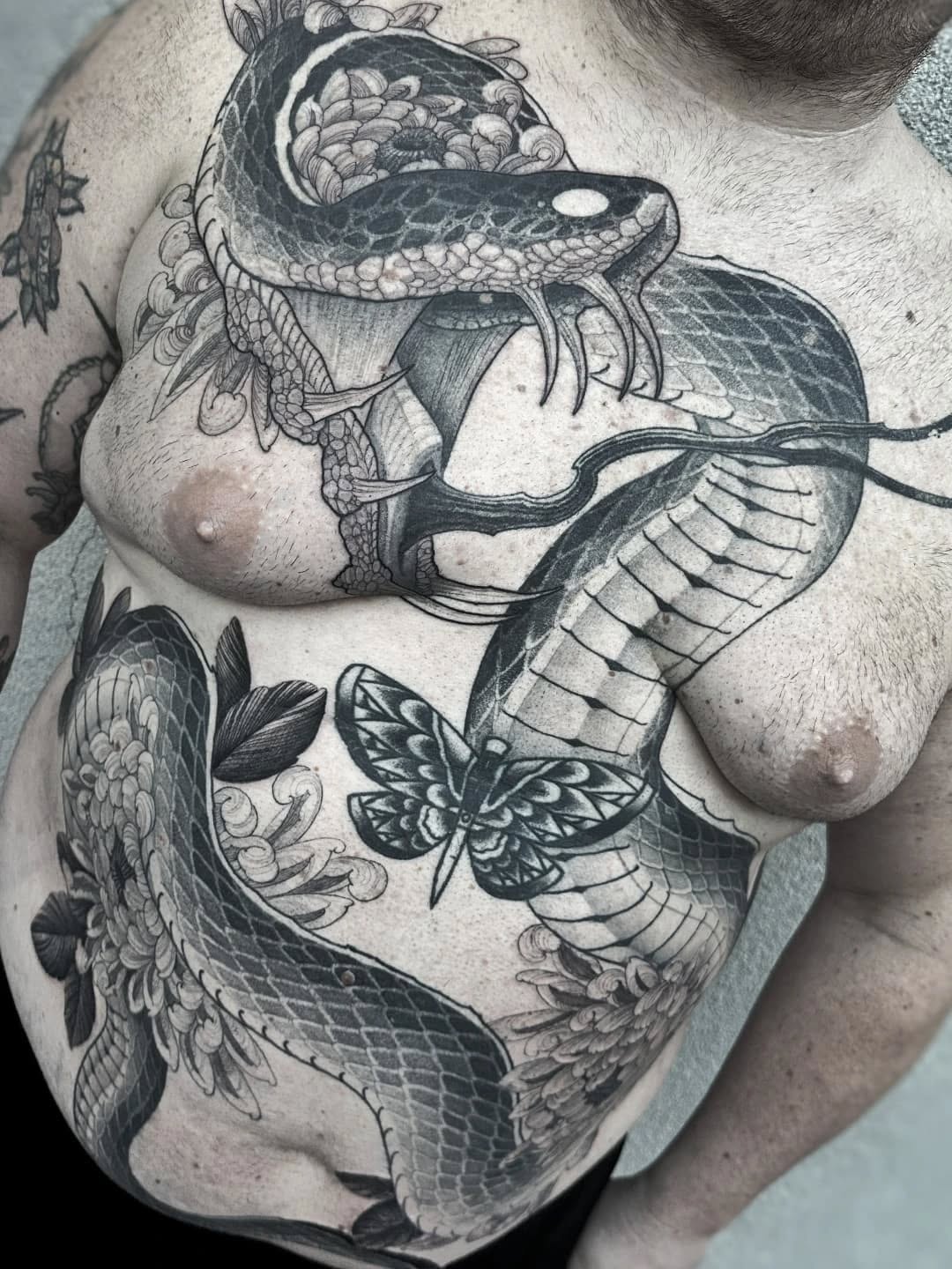 Large detailed chest tattoo featuring an orca whale with ornate floral and scroll details, accompanied by a moth and additional marine elements in black ink.
