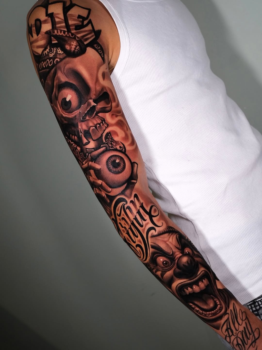 Full-sleeve arm tattoo featuring skulls, eyes, demons, and script lettering in brown and black ink on tan skin.