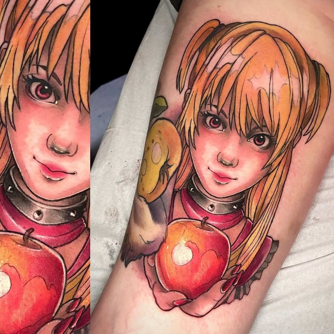 Colorful tattoo on forearm featuring an anime-style girl with orange hair, pink cheeks, and large eyes, holding a red apple with gold accents.