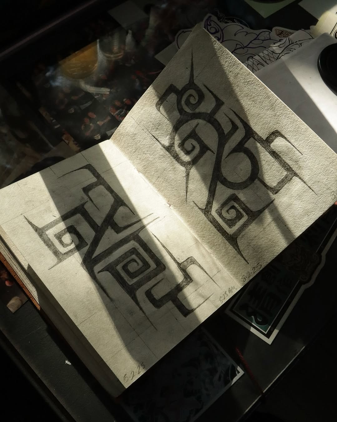 Sketchbook pages displaying geometric spiral and angular symbol designs in black ink on white paper under natural light.