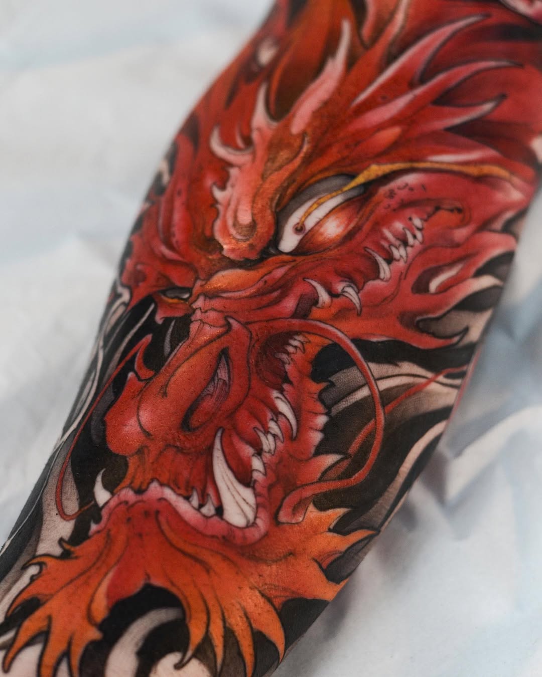 Red and orange demon or oni face with detailed features and flowing hair covering an arm, displayed on light skin.