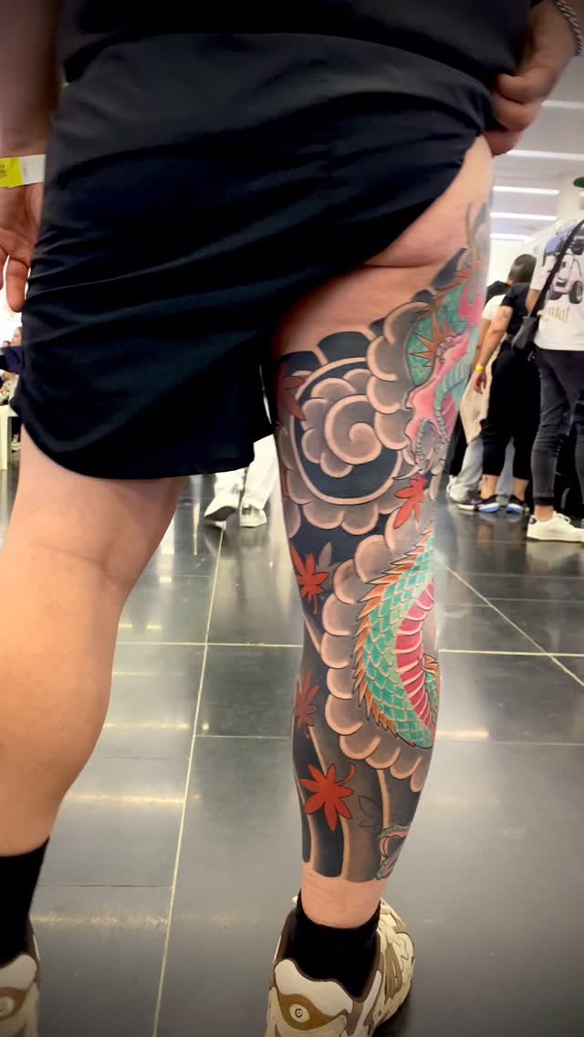 Full leg tattoo sleeve featuring colorful flowers, leaves, and circular cloud motifs in red, green, and brown tones on dark background.