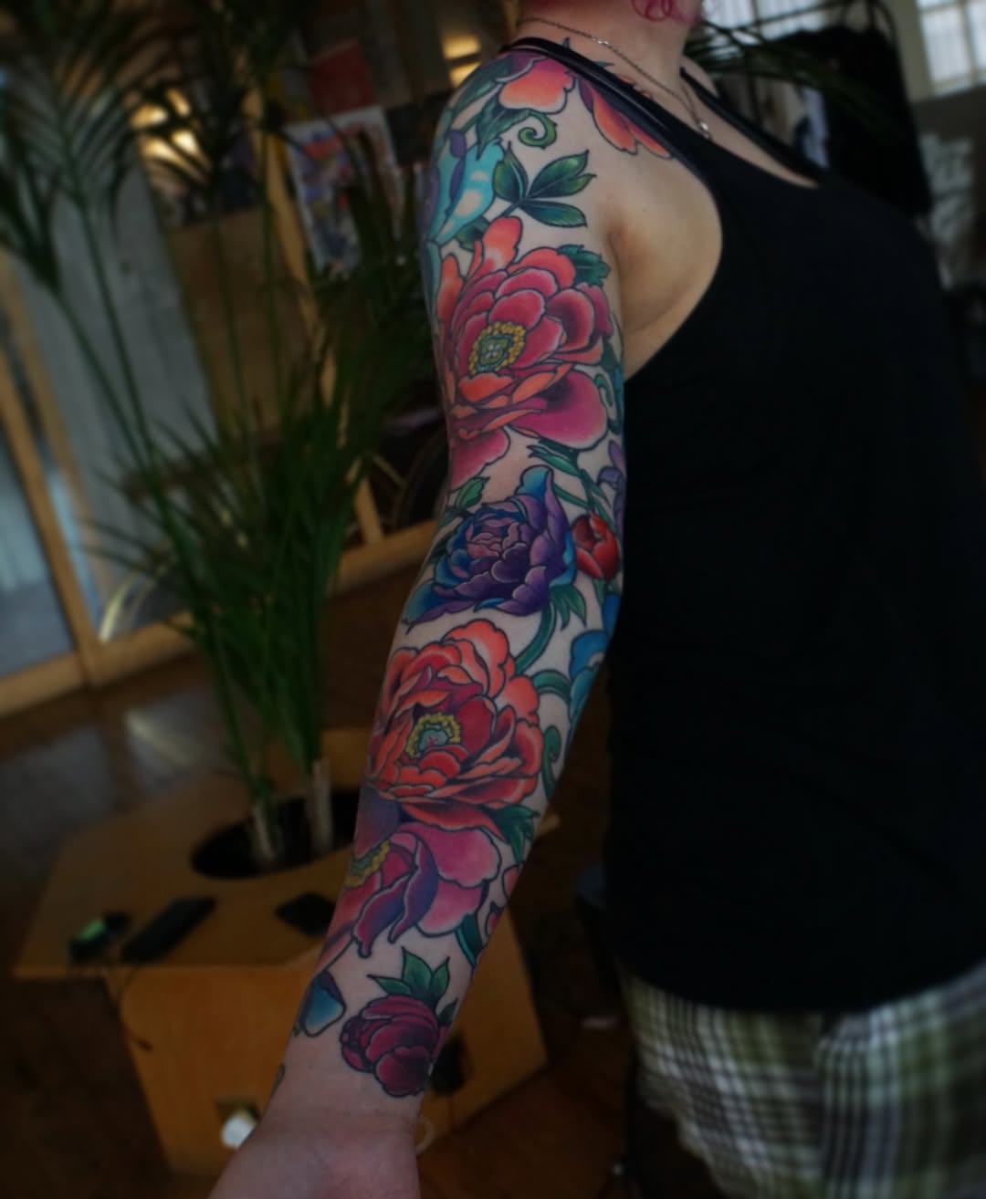 Full-length arm sleeve tattoo featuring multiple red and purple flowers with green leaves and blue accents on a person's right arm.