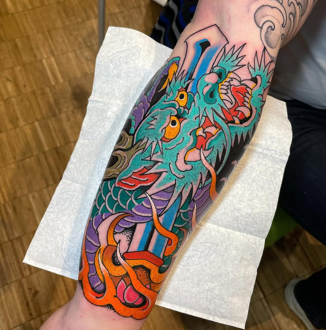 Colorful dragon head tattoo on forearm featuring turquoise, purple, orange, and red with detailed scales and spiky features, displayed on white protective paper.