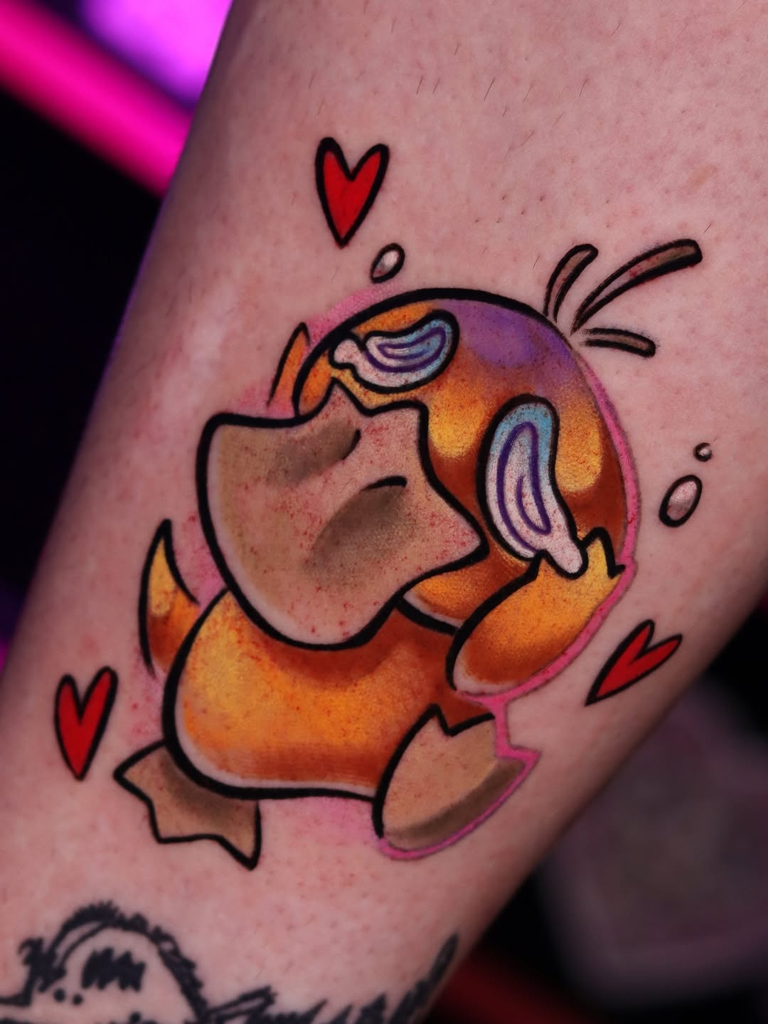 Colorful tattoo on arm featuring a cheerful character in orange clothing with hearts, surrounded by purple and pink shading and small red hearts.