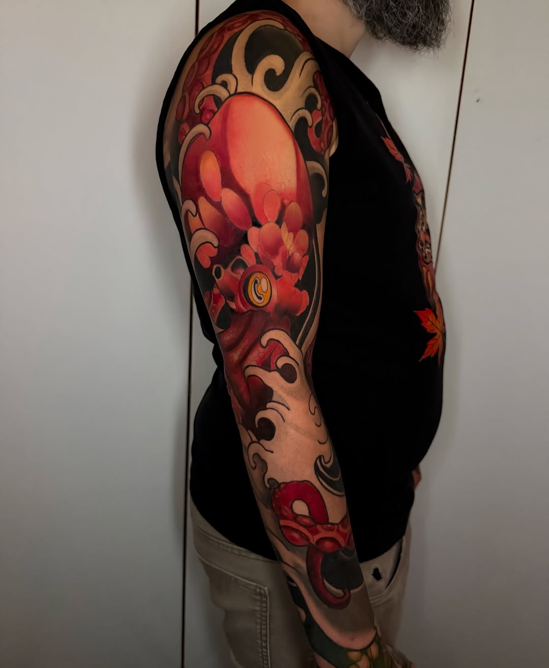 Full sleeve tattoo featuring a large red lantern with ornamental scrollwork and flowering branches in red, orange, and tan tones on the upper arm.