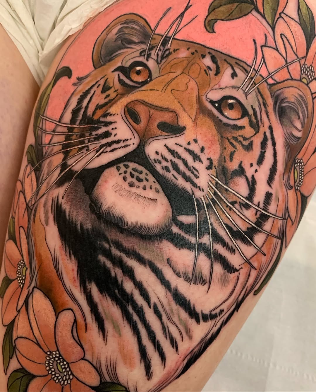Tiger head with whiskers and stripes surrounded by orange flowers on skin with coral and pink background tones.