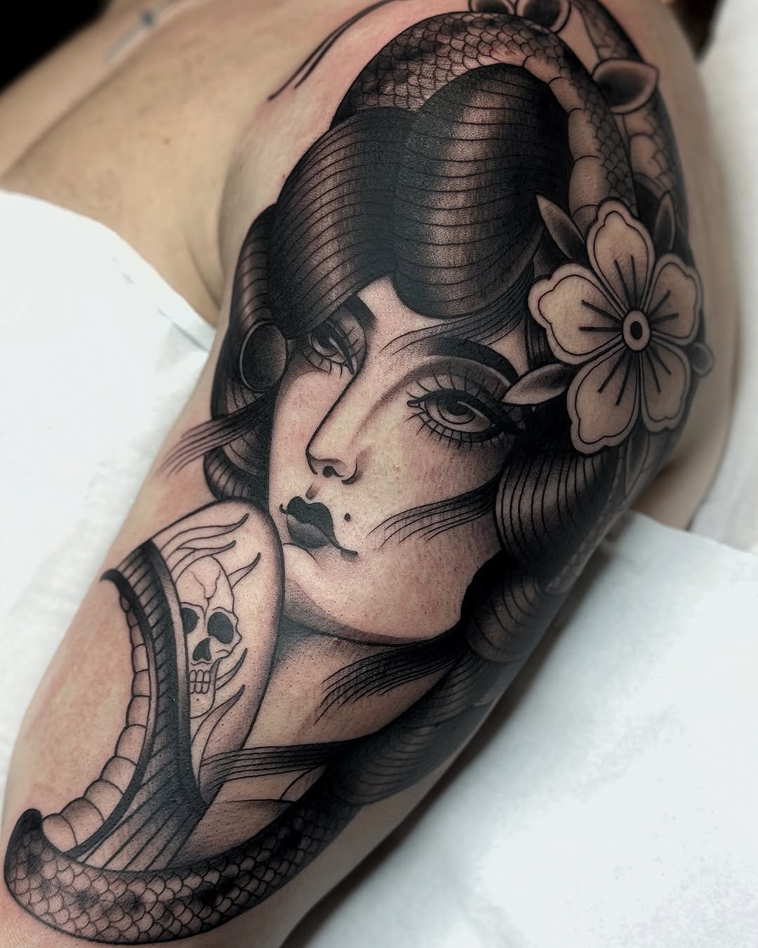 Woman's portrait with flowing hair, flowers, and serpent wrapped around arm, rendered in black ink on upper leg.