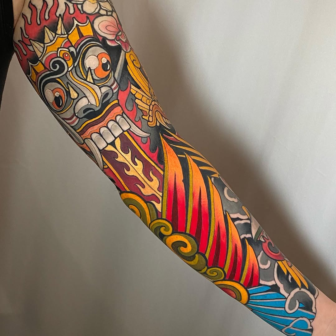 Colorful full-length arm sleeve tattoo featuring a skull with flames, ornamental scrollwork, and water waves in red, orange, yellow, black, and blue.
