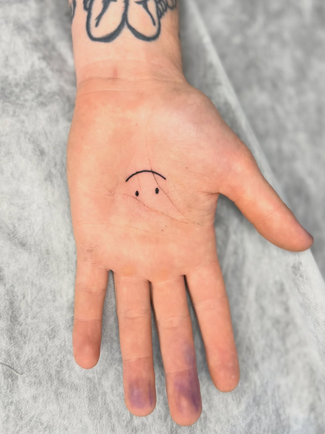 Simple line-drawn sad face tattoo on the palm of an open hand with black ink.
