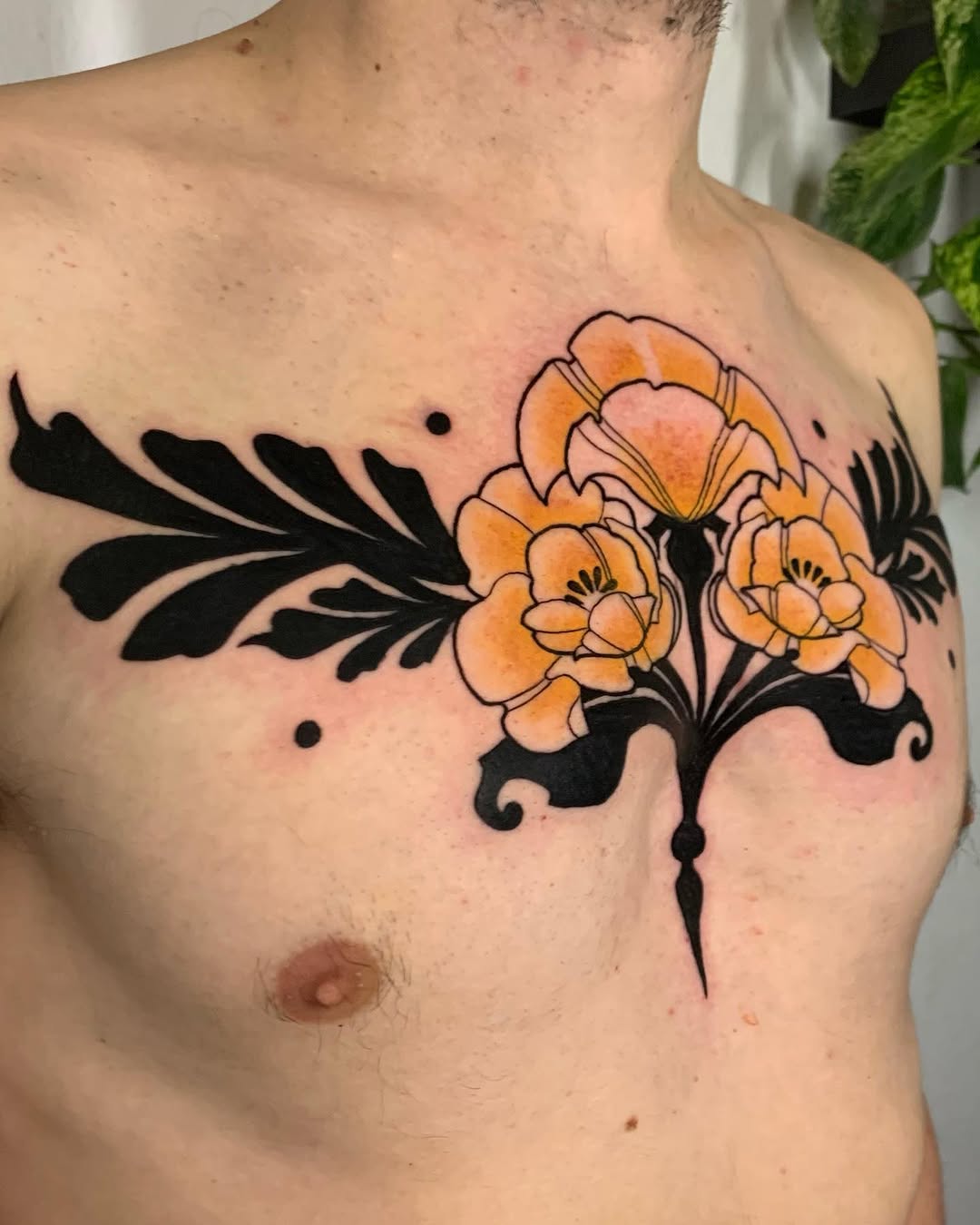 Chest tattoo featuring orange flowers with black ornamental leaf designs and decorative flourishes on male torso.