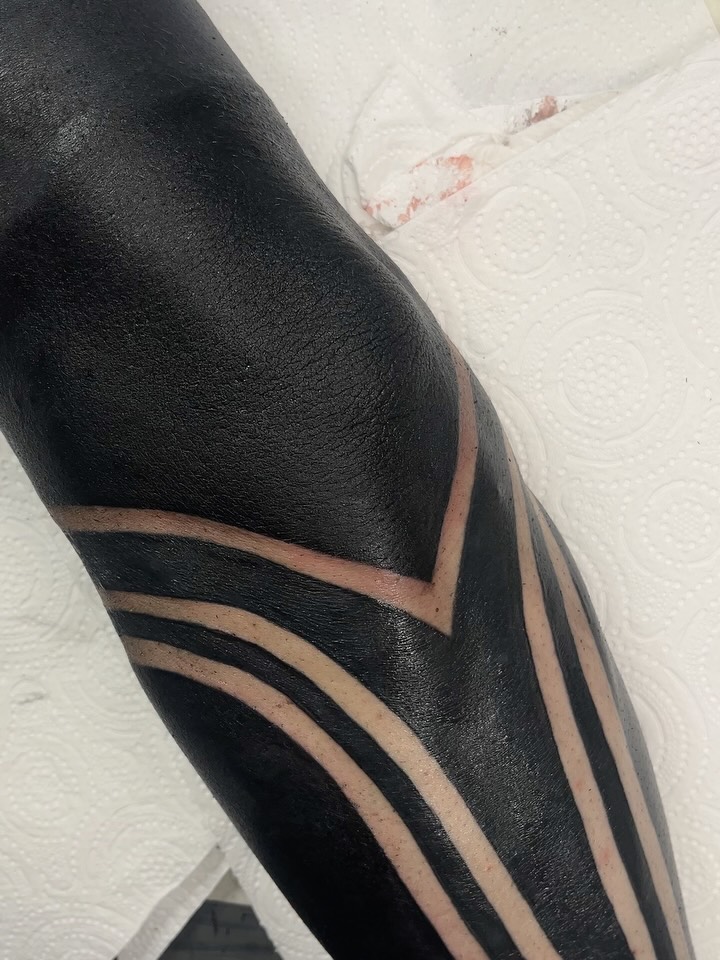 Geometric tattoo on upper arm featuring black filled shapes with tan curved lines creating angular patterns.