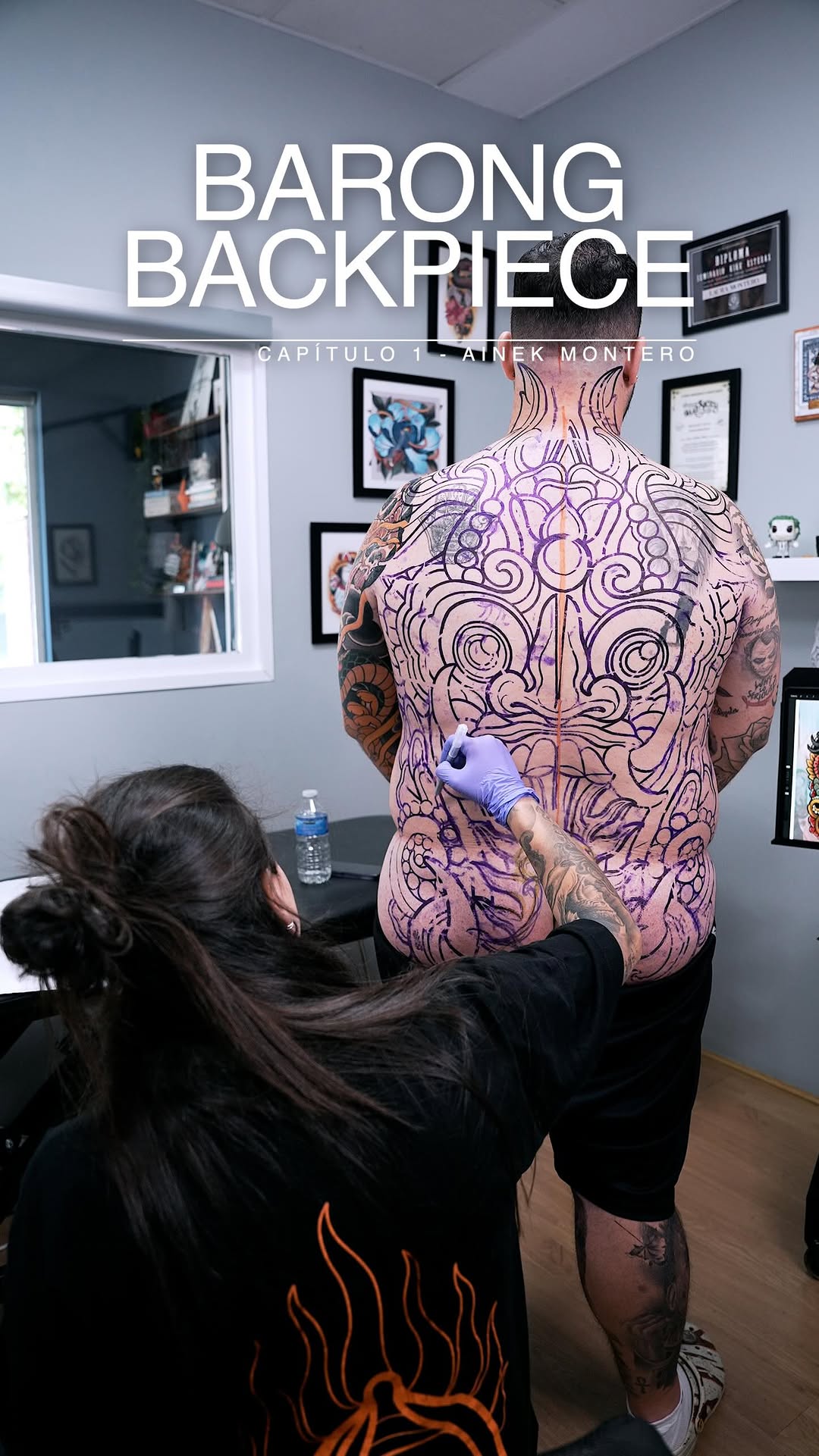 Tattoo artist applies purple and black intricate skull design with ornamental details across client's entire back in studio setting.