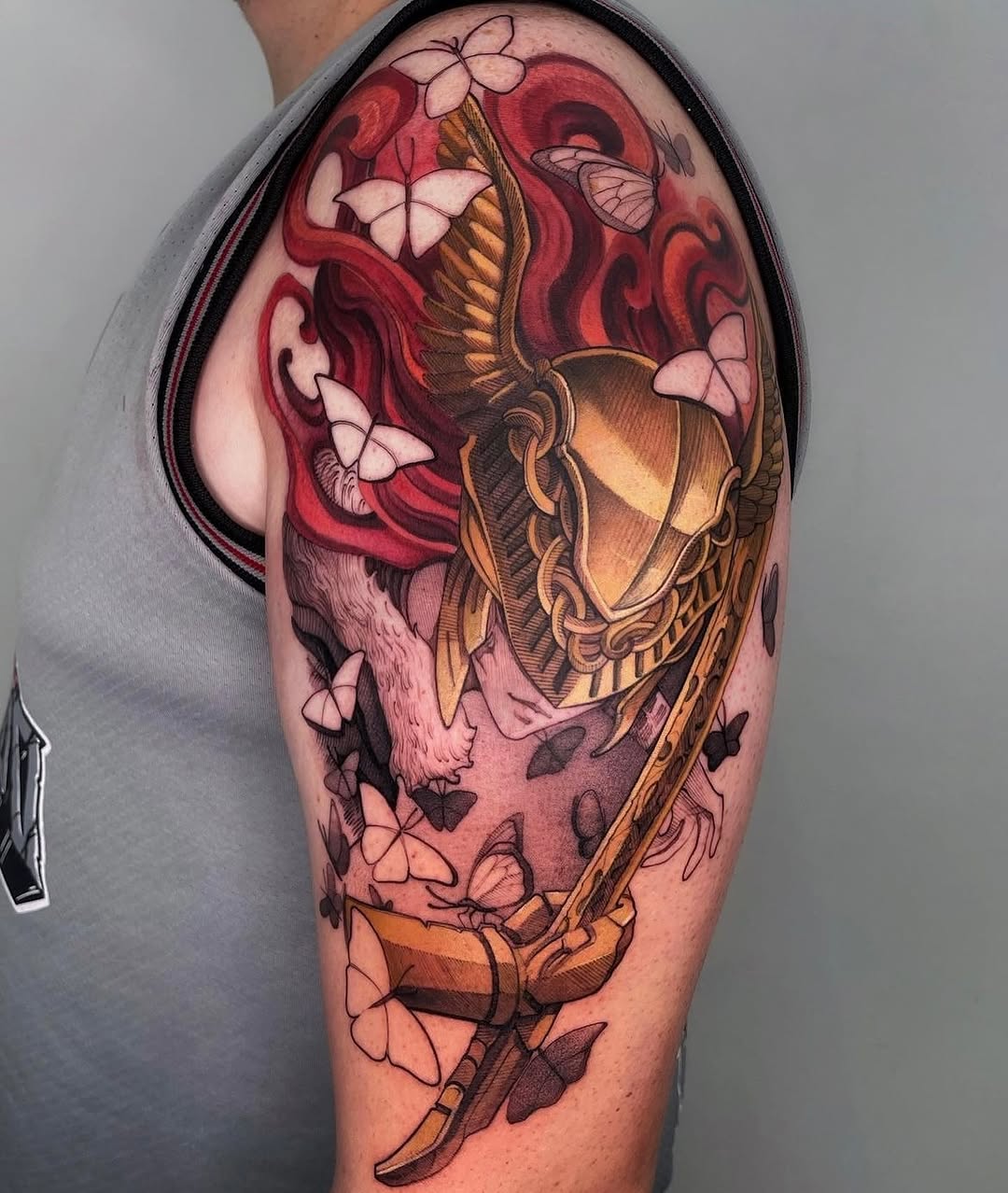 Colorful shoulder tattoo featuring a skull with red flames, golden lantern, butterflies, and flowing ribbons in warm and cool tones.