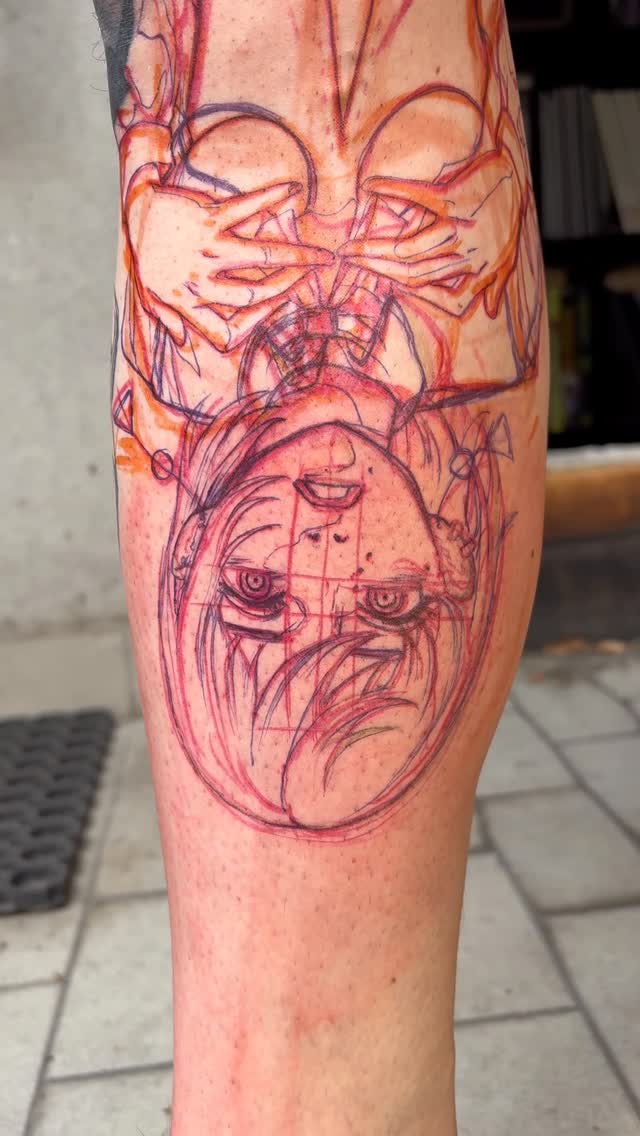 Fresh red and purple ink tattoo on a calf featuring stacked expressive faces with exaggerated features and flowing line work.