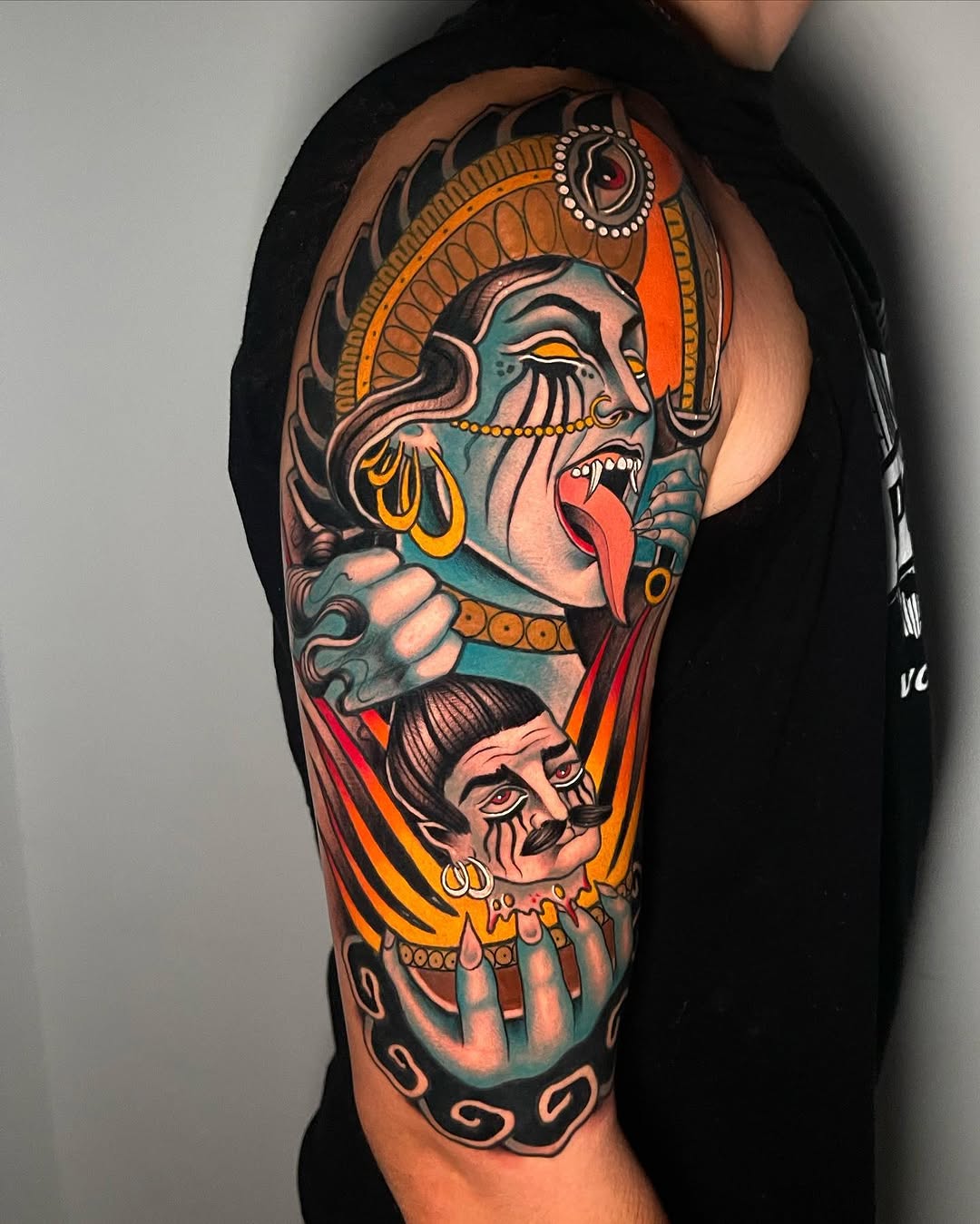 Colorful arm sleeve tattoo featuring two stacked face designs with ornate headdresses, jewelry, and open mouths in orange, teal, and gold tones.
