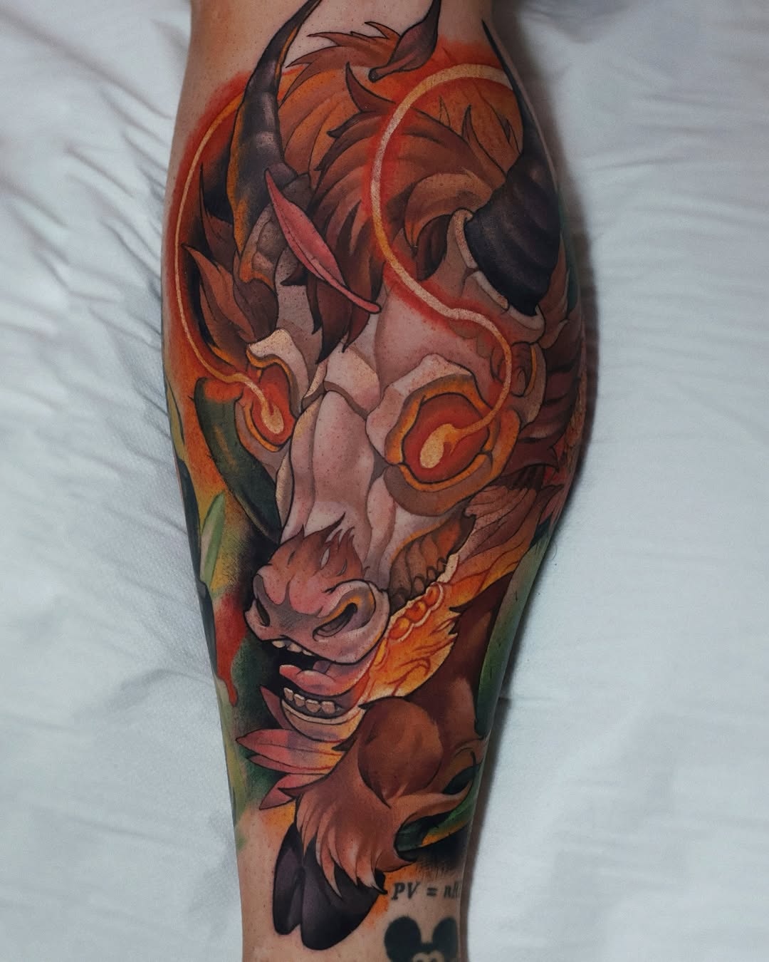 Colorful oni mask tattoo on calf featuring orange and red flames, dark shadows, and ornate details with green accents.