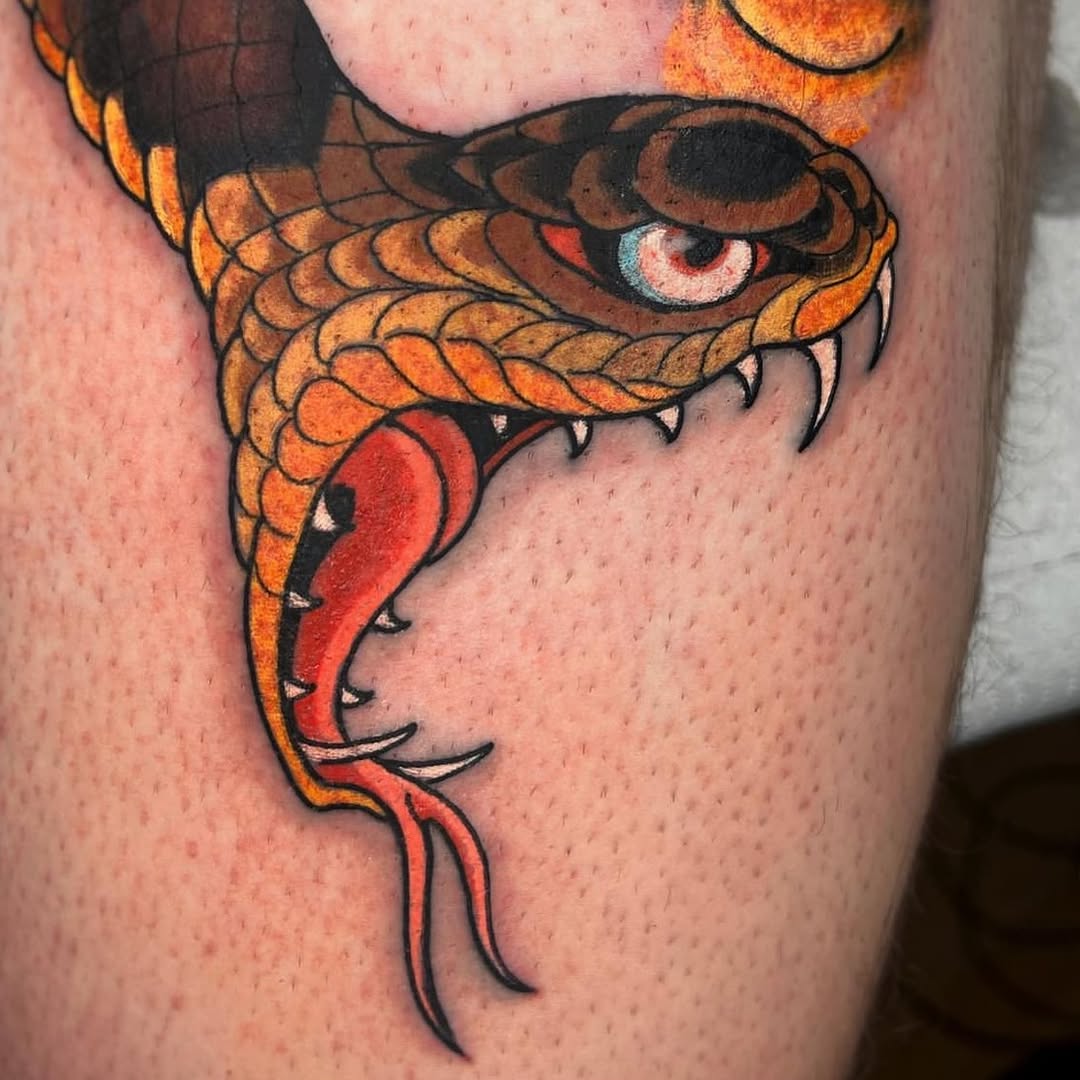 A colored snake tattoo with orange and red scales, black outlines, and detailed eyes on the upper thigh area.