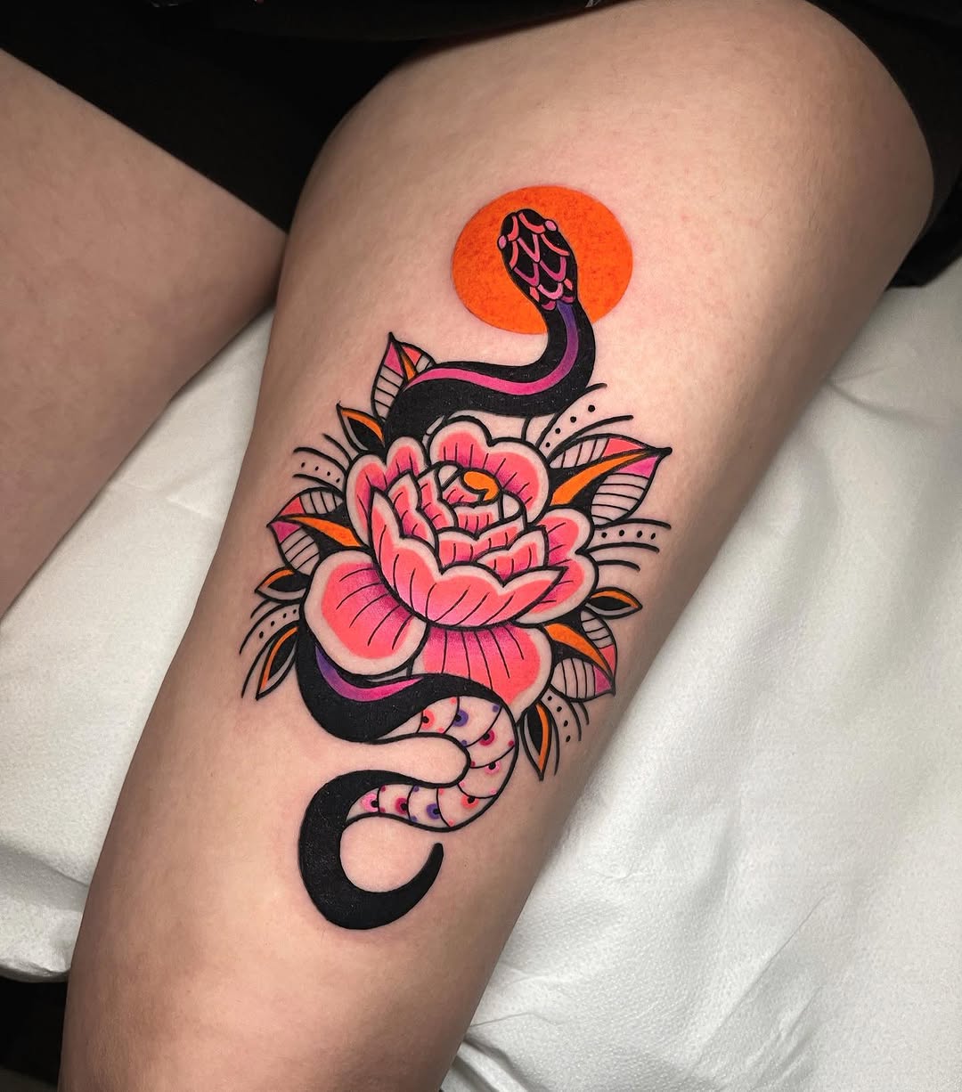 Colorful leg tattoo featuring a pink peony flower with black serpents, orange sun, and decorative leaves in orange, purple, and pink hues.