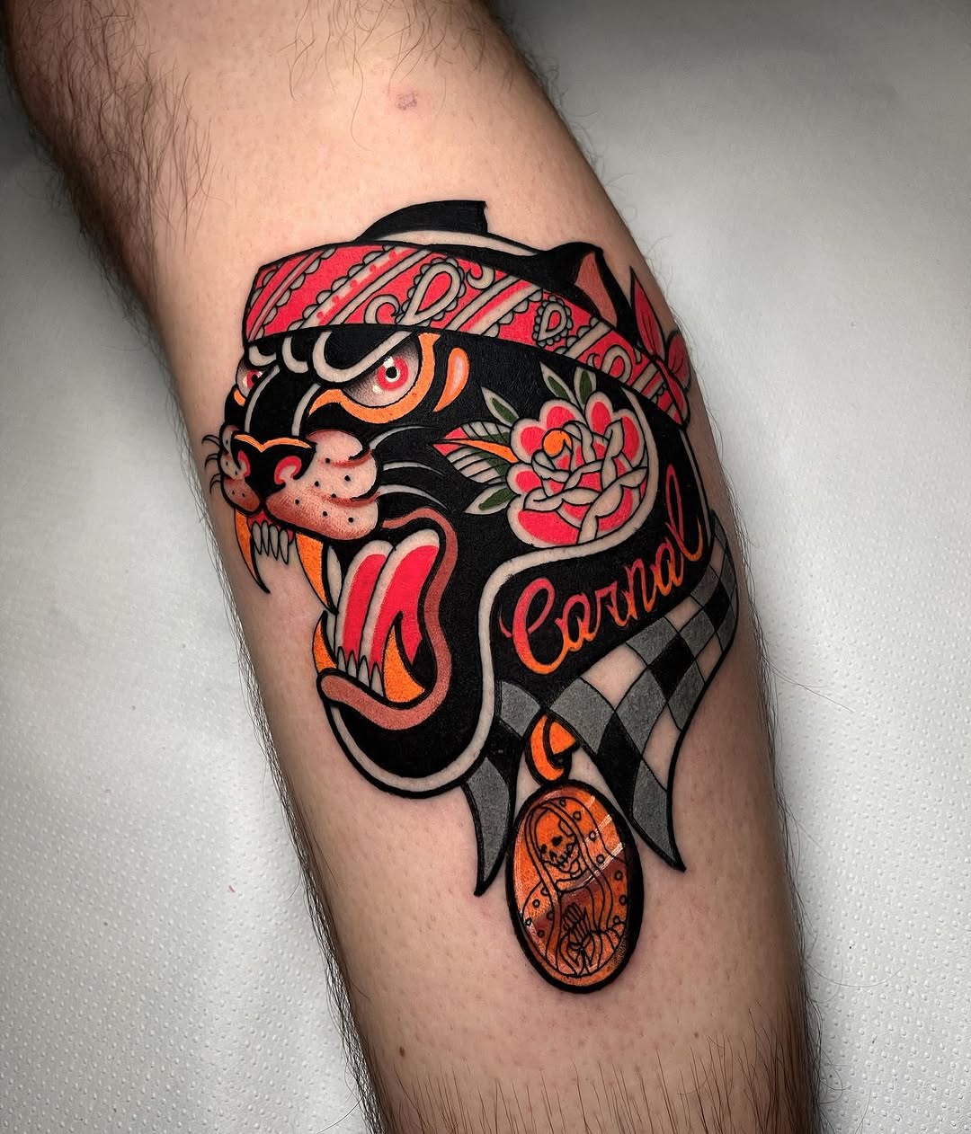 Colorful tiger head tattoo with red bandana, orange stripes, pink flower, and ornate pendant on lower leg.