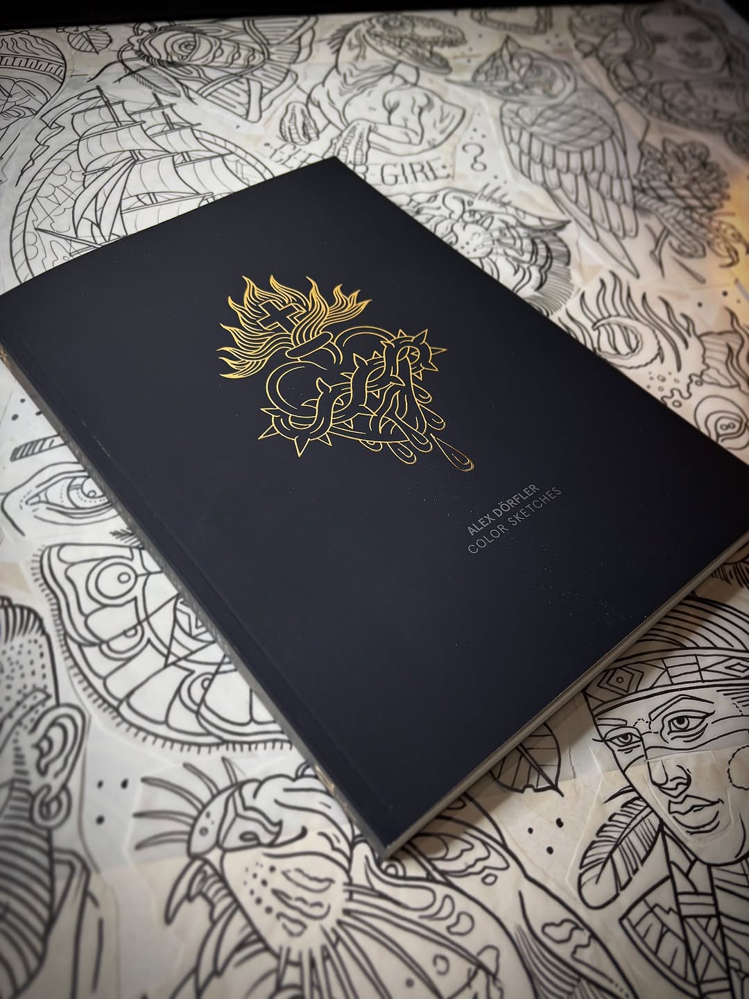 Black cover book with gold lion and serpent design displayed on pages of intricate line art sketches.