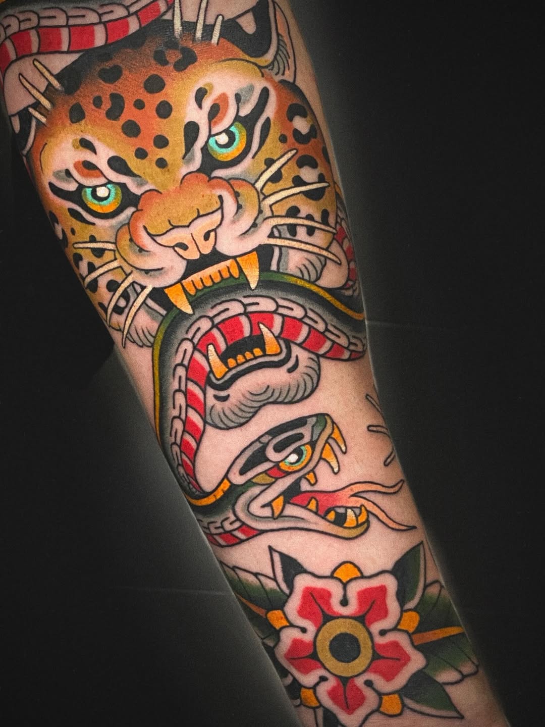 Colorful arm sleeve tattoo featuring a leopard head, snake, roaring tiger mask, and floral design in orange, red, yellow, and green.