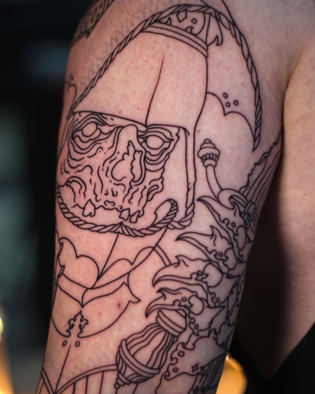 Skull with rope border and jellyfish designs in black outline on upper arm and shoulder area.