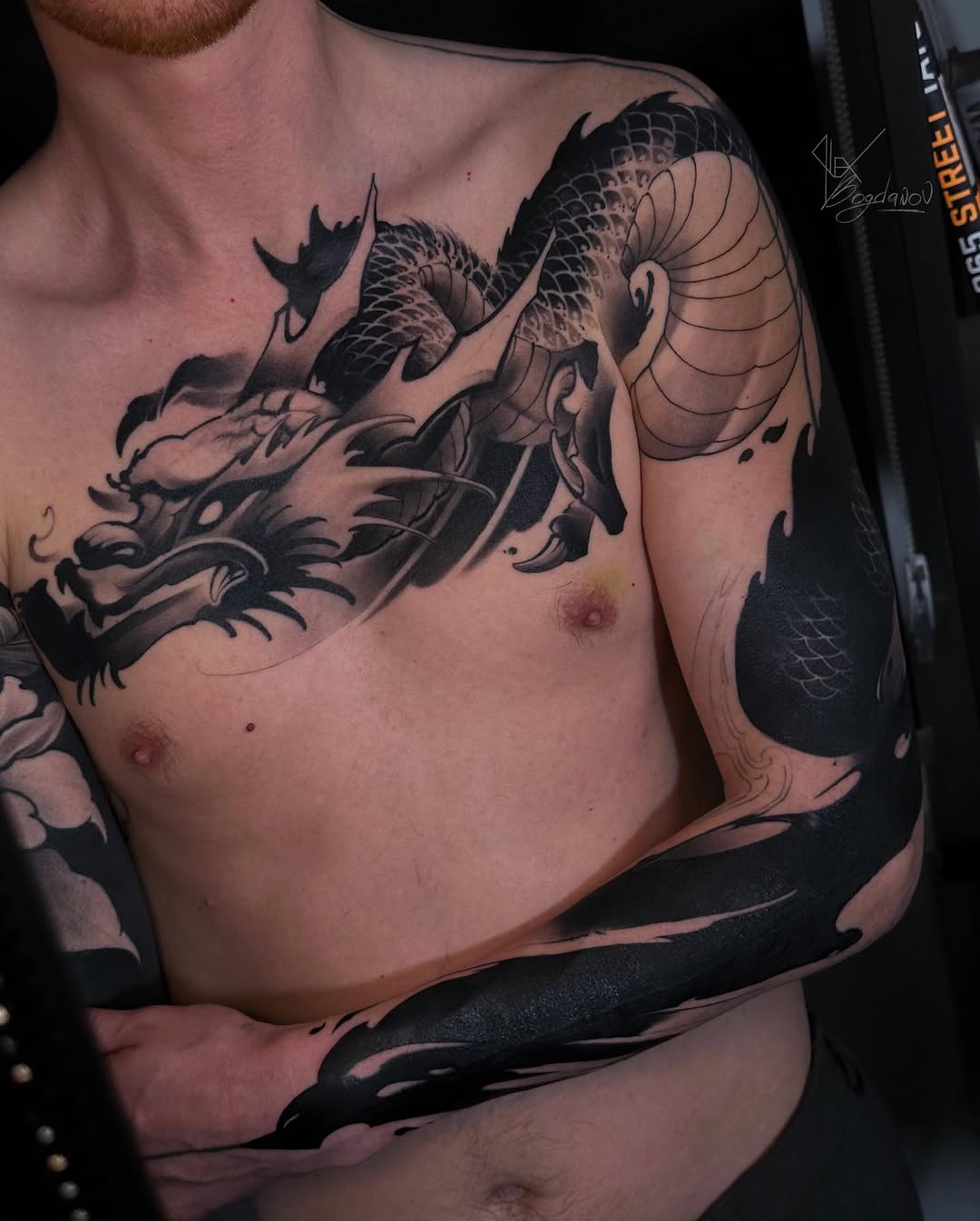 Large dragon tattoo wrapping across chest and right arm in black ink with detailed scales and facial features.