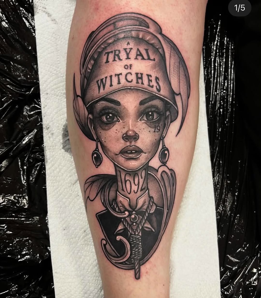 Portrait tattoo on forearm depicting a woman wearing a bonnet labeled "Trial of Witches" with ornate decorative elements below, rendered in black and grey ink.