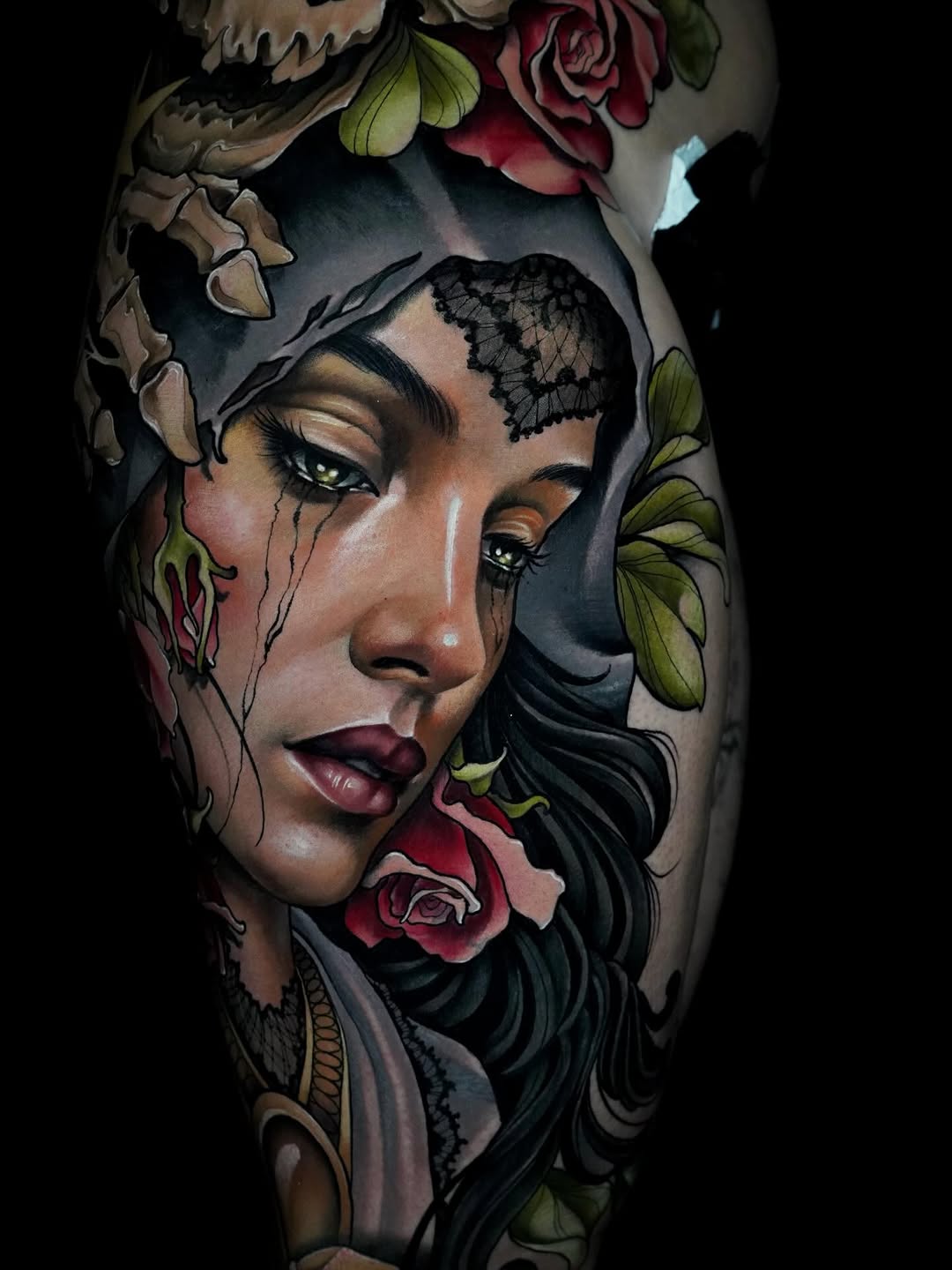 Colored tattoo on leg featuring a woman's face with tears, lace forehead detail, and surrounding flowers in red, green, and gold tones.