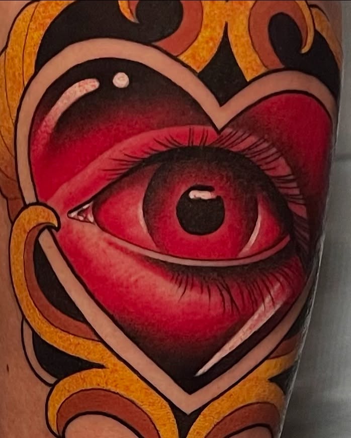 Red eye and lips within a red heart surrounded by orange and black decorative swirls, tattooed on skin.