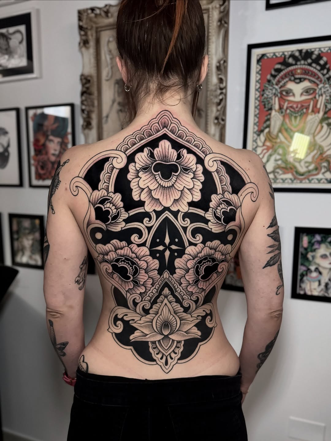 Back tattoo featuring a symmetrical skull with ornate floral designs, scrollwork, and geometric patterns in black and tan ink.