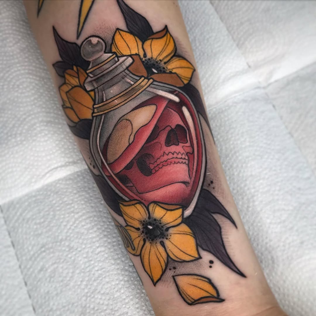 Tattoo on an arm featuring a potion bottle with a skull inside, surrounded by yellow flowers and dark leaves, rendered in red, orange, black, and gray tones.