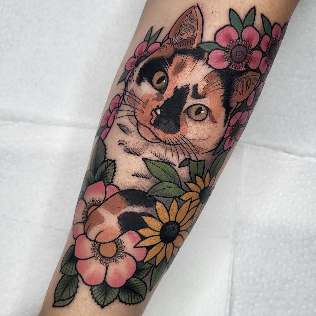 Calico cat head with pink and yellow flowers surrounding it on a forearm, featuring orange eyes and black markings.