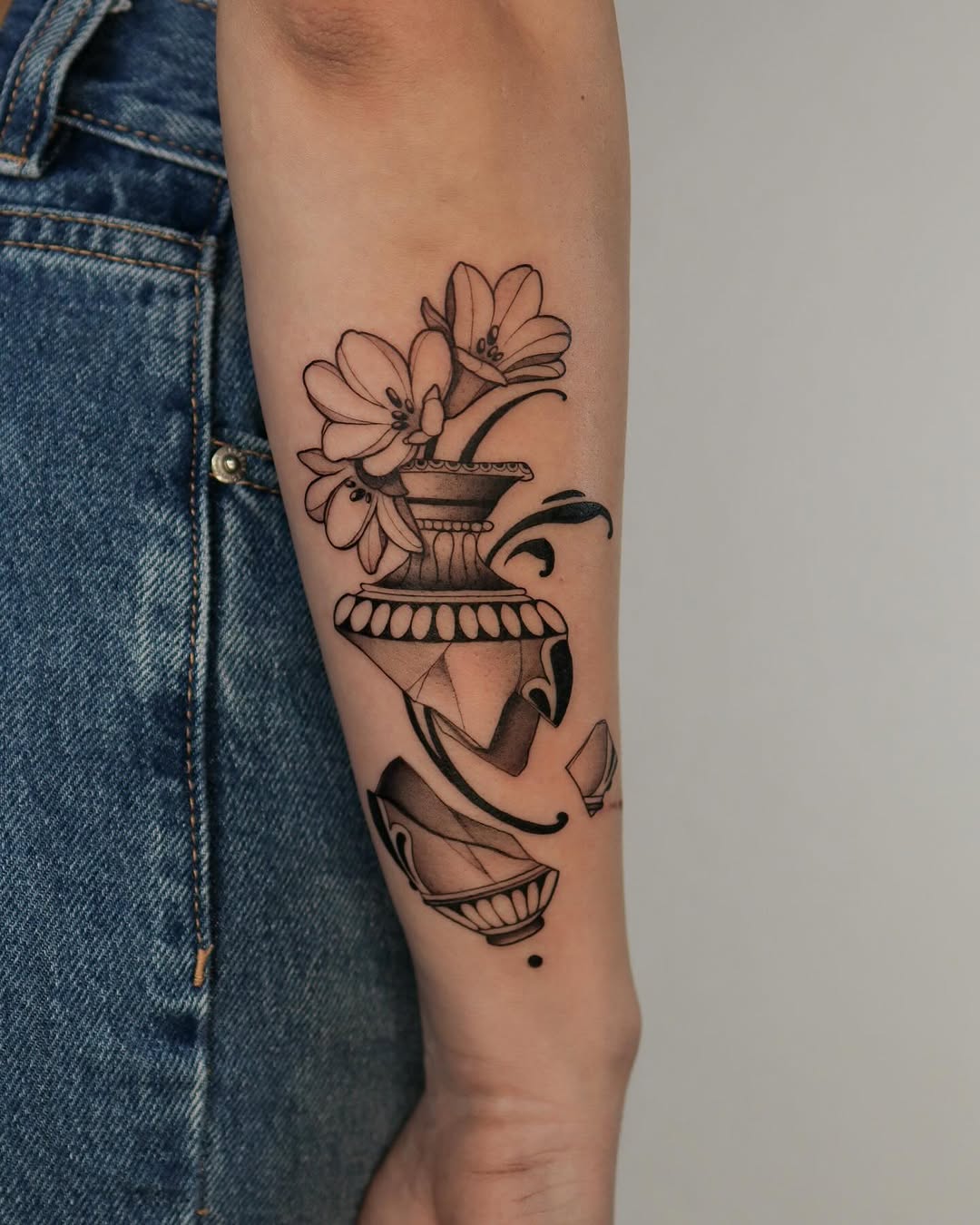 Stacked decorative urns and vessels with flowers blooming from the top vessel, outlined in black ink on the inner forearm.