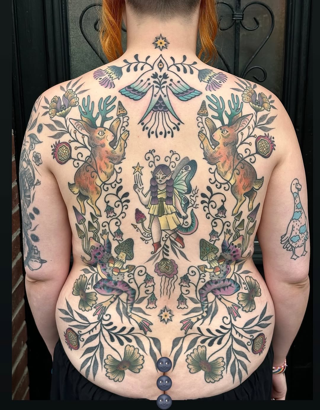 Back tattoo featuring a winged fairy surrounded by deer, flowers, jellyfish, and ornamental swirls in teal, purple, brown, and black ink.