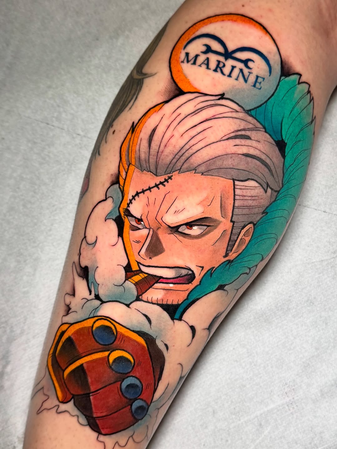 Colorful tattoo on a calf featuring an orange-faced character with gray hair, a heart-shaped speech bubble reading "MARINE," teal wings, and a red fist below.