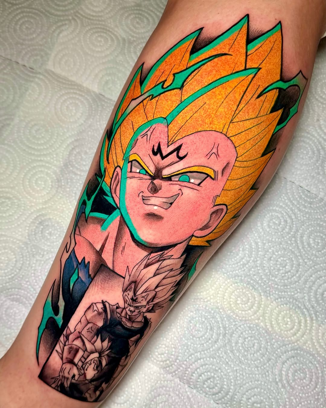 Colorful tattoo on a forearm featuring a pink-faced character with spiky orange hair, green outlines, and blue clothing, with smaller figures below.