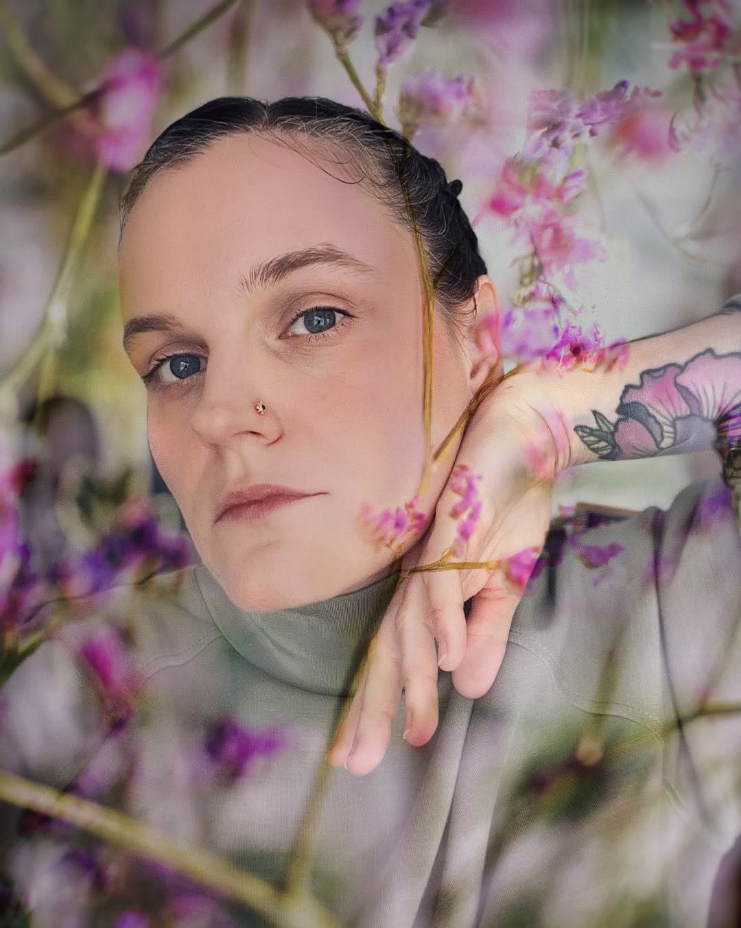 Woman displaying a floral tattoo on her upper arm featuring pink and purple flowers with green leaves in muted tones.
