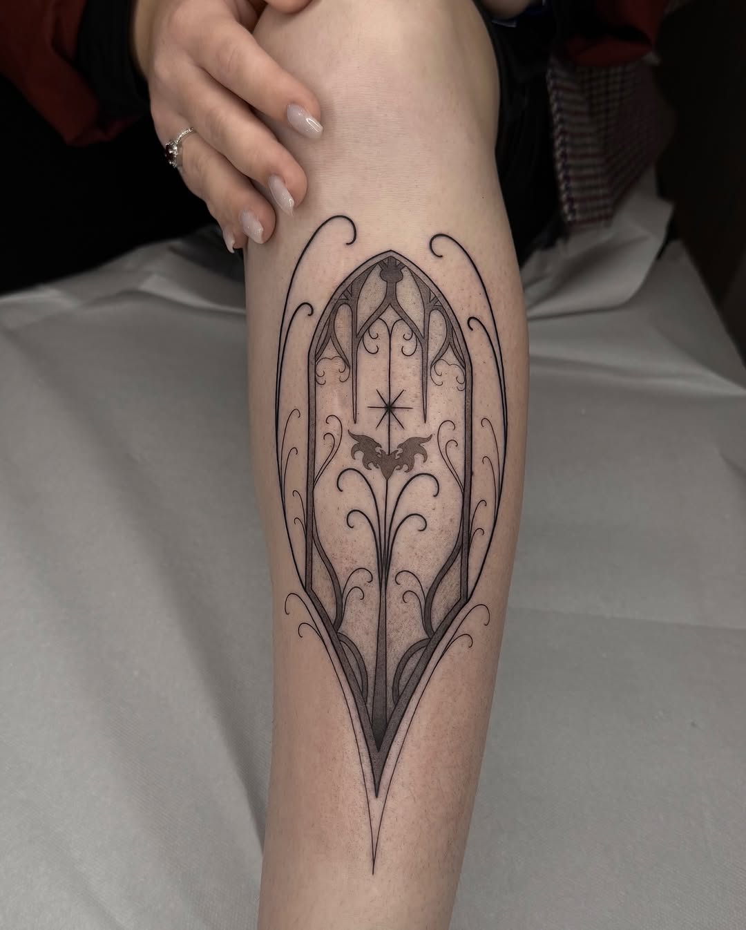 Gothic ornate gate design with bat and star motif tattooed on the inner forearm in black ink with detailed linework and shading.