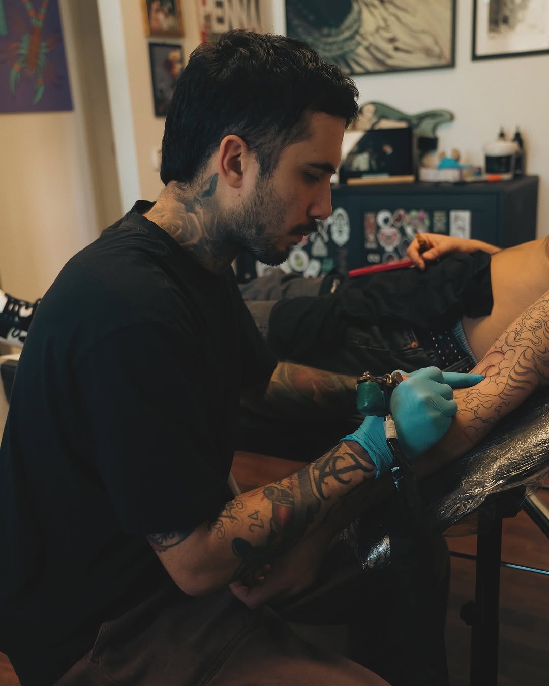 Tattoo artist in black gloves applies ink to client's arm featuring geometric and decorative designs in black and orange.
