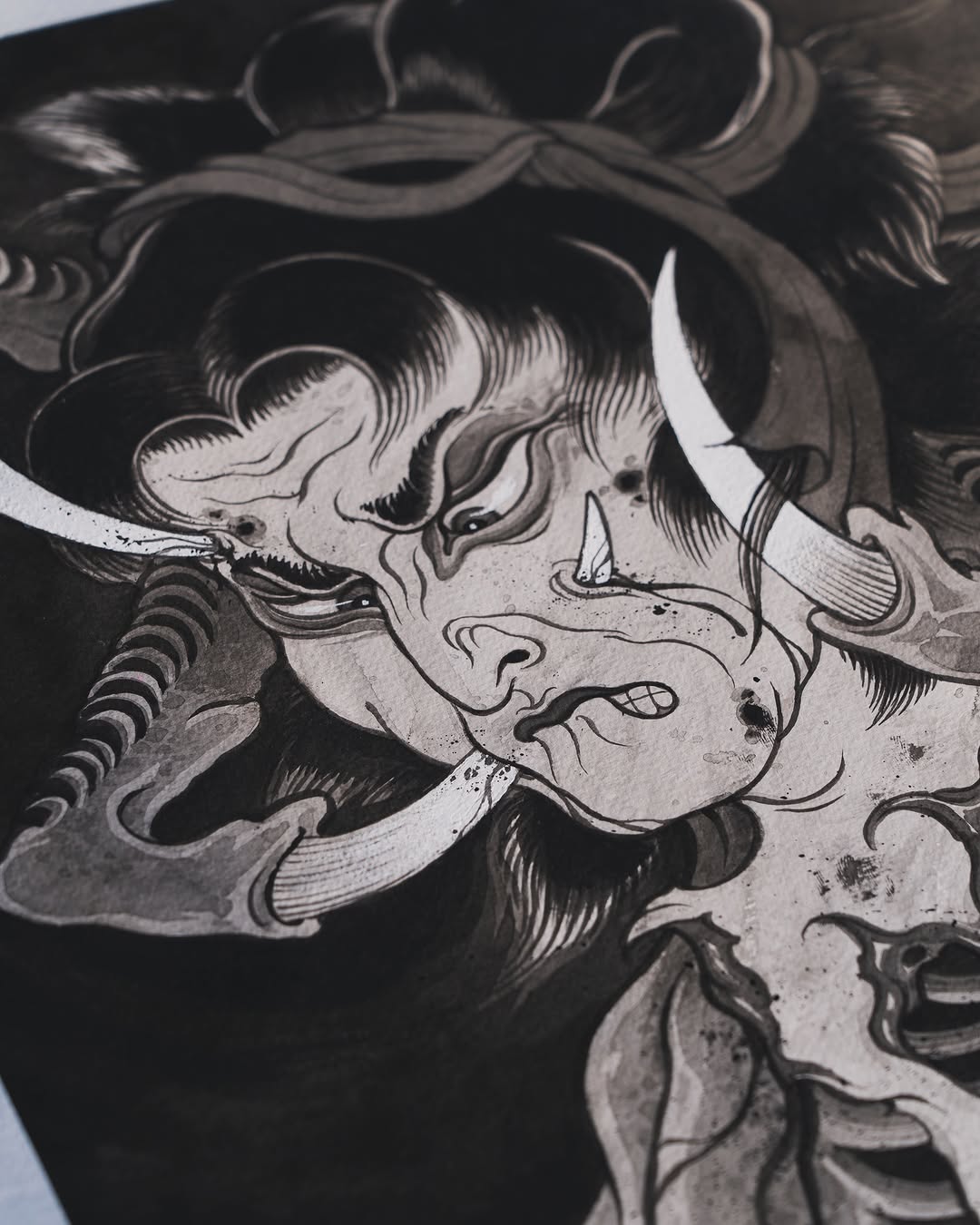 Detailed demon face tattoo design with horns, fangs, and flowing hair rendered in black ink and grayscale shading on paper.