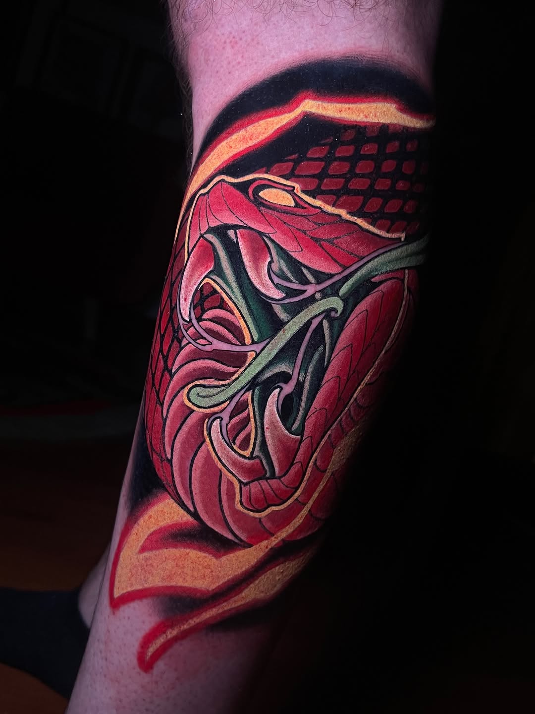 Vibrant red and gold anatomical heart tattoo on the calf with black outlines and decorative flourishes.