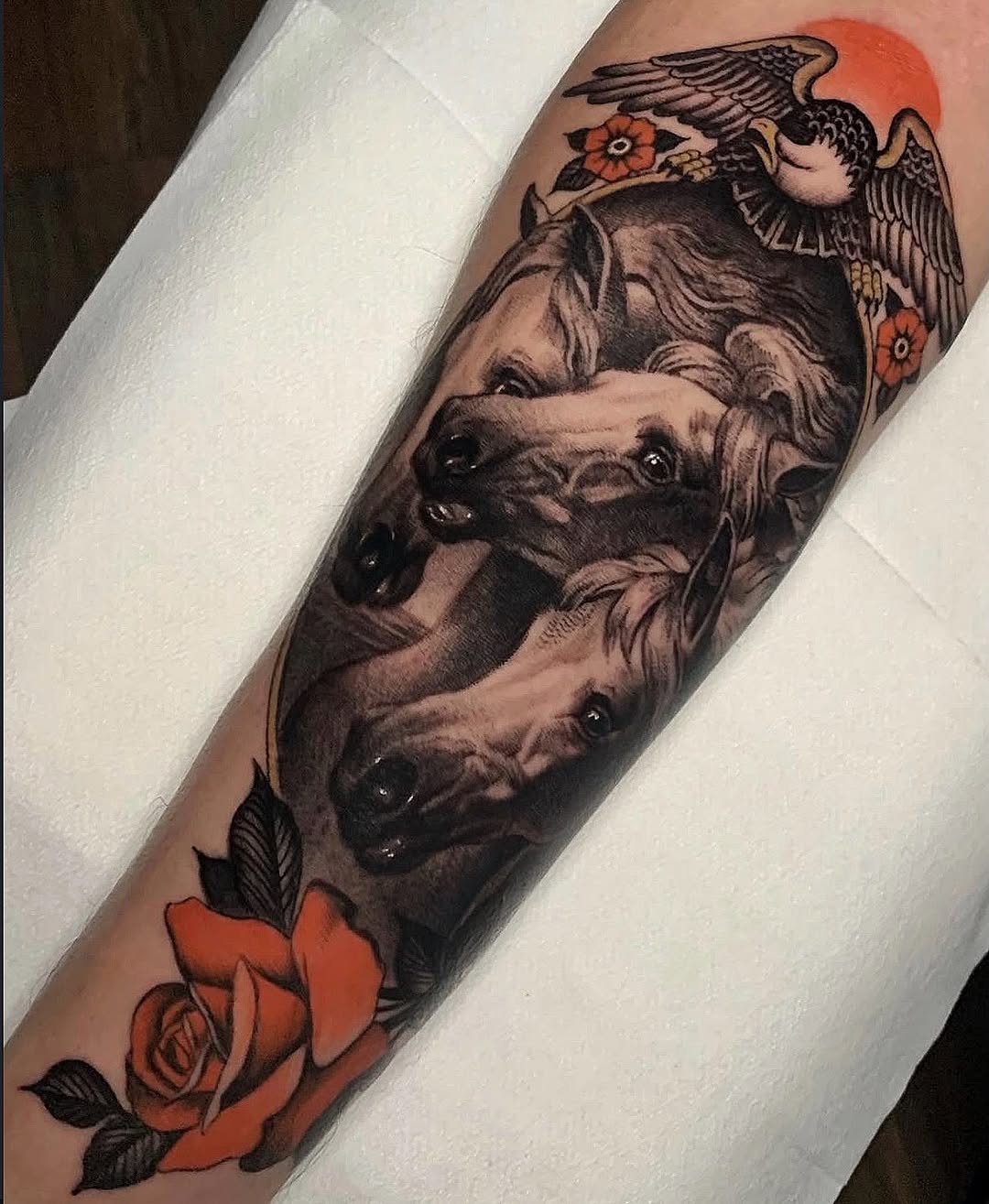 Two dogs' heads with angels and red flowers on an arm, featuring a red sun and orange roses in the composition.