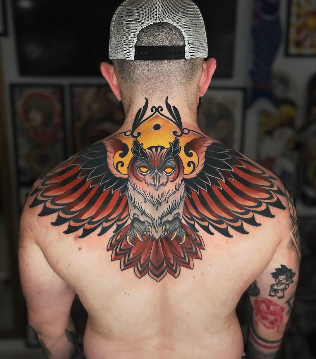 Detailed colored owl with spread wings and ornamental designs spanning the upper back and shoulders, featuring red, orange, black, and yellow tones.