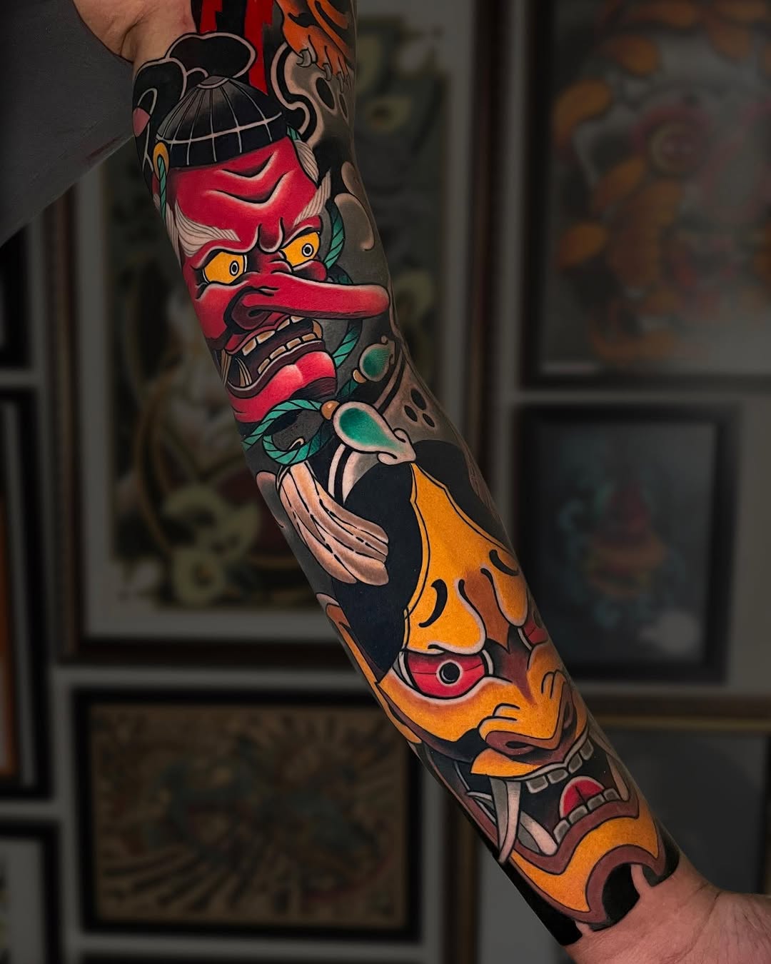 Colorful sleeve tattoo featuring stacked demon and mask faces with red, orange, and teal details on a person's arm.